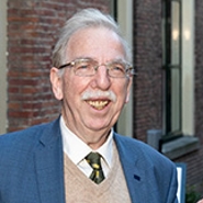Een vriendelijk lachende oudere man met een bril en een snor