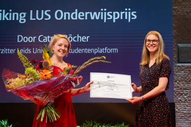 A smiling Emily Strange holds a large bunch of flowers and receives the teaching prize certificate from the chair of the Leiden University Student Platform.