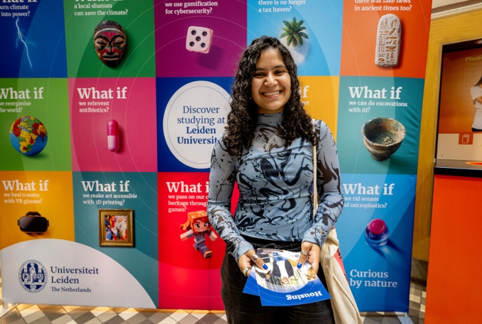 Een meisje met blauw -zwart shirt en zwart haar staat voor de campagneposters van de universiteit met daarop 'what if'geschreven.