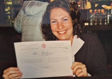 A headshot of a smiling Ellen Buschman holding her psychology degree certificate.