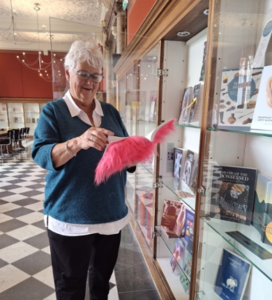 Beadle Tineke Schutte stands next to a display cabinet and holds a book bound in hot pink faux fur.