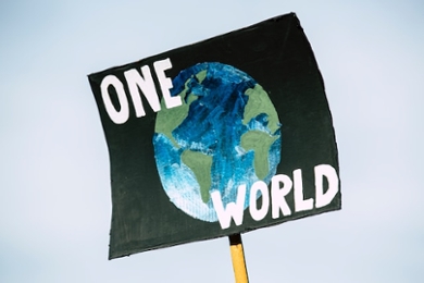 Afbeelding van een protestbord tijdens een klimaatdemonstratie met daarop de tekst 'One World'