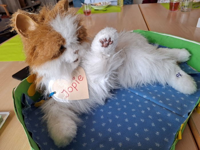 A social robot in the form of a cuddly cat lies outstretched in a hand-made cat basket.