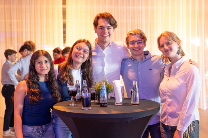 Studenten staan aan een stafel en kijken vrolijk in de camera.