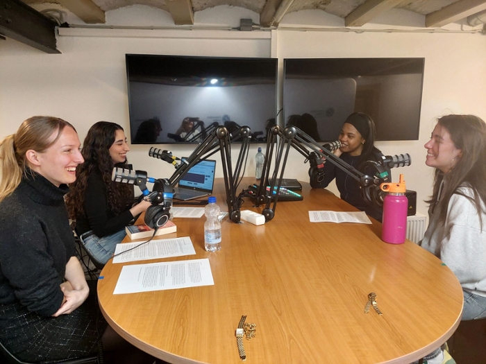 Vier vrouwelijke studenten zitten aan een tafel en nemen een podcast op. Ze ogen vrolijk en glimlachen. Ze hebben elk een script voor zich liggen. De podcast maakt deel uit van hun deelname aan het Honours-programma van de Faculteit der Rechtsgeleerdheid.