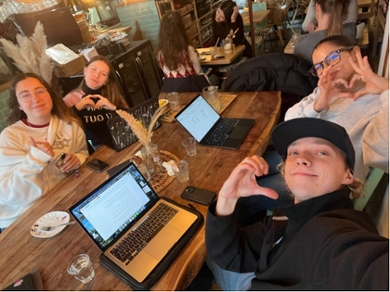Group of four anthropology students sitting with their laptops in a cafe making heart gestures with their hands.