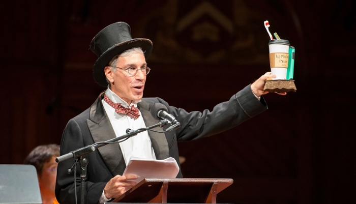 Marc Abrahams, wearing a high hat, holds an Ig Nobel prize: a coffee cup with a toothbrush inside.
